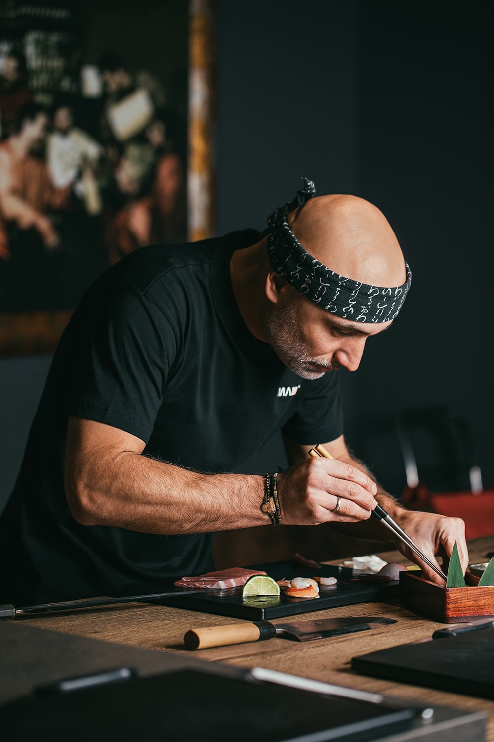 Fotografía gastronómica de chef preparando sushi con pinzas sobre tabla negra en restaurante, escena culinaria con enfoque editorial