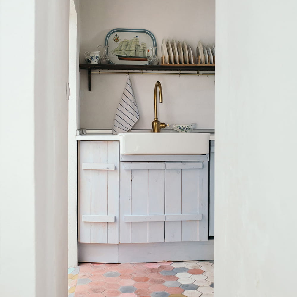 Fotografía de interiores de cocina mediterránea con muebles blancos, grifería dorada y suelo hidráulico