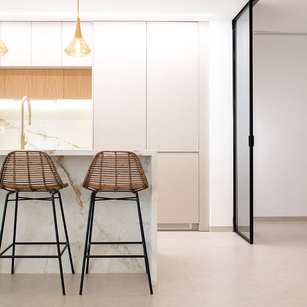 Fotografía de interiores de cocina moderna con isla efecto mármol, taburetes de ratán y puerta de cristal