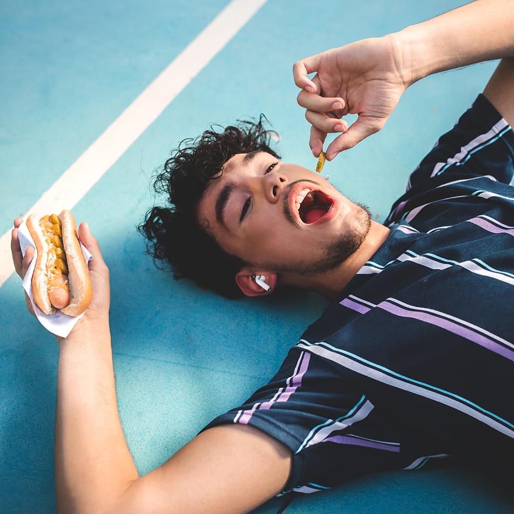 Fotografía lifestyle publicitaria con modelo masculino en pista deportiva comiendo perrito caliente para campaña de marca