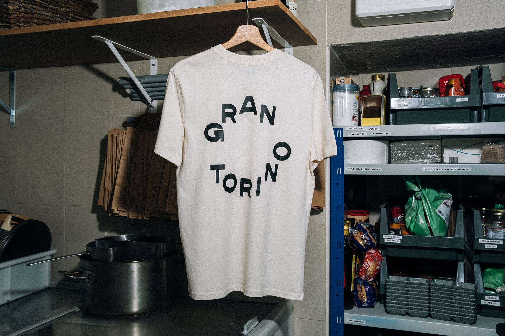 Fotografía gastronómica de camiseta del restaurante italiano Gran Torino colgada en cocina profesional con estanterías y utensilios
