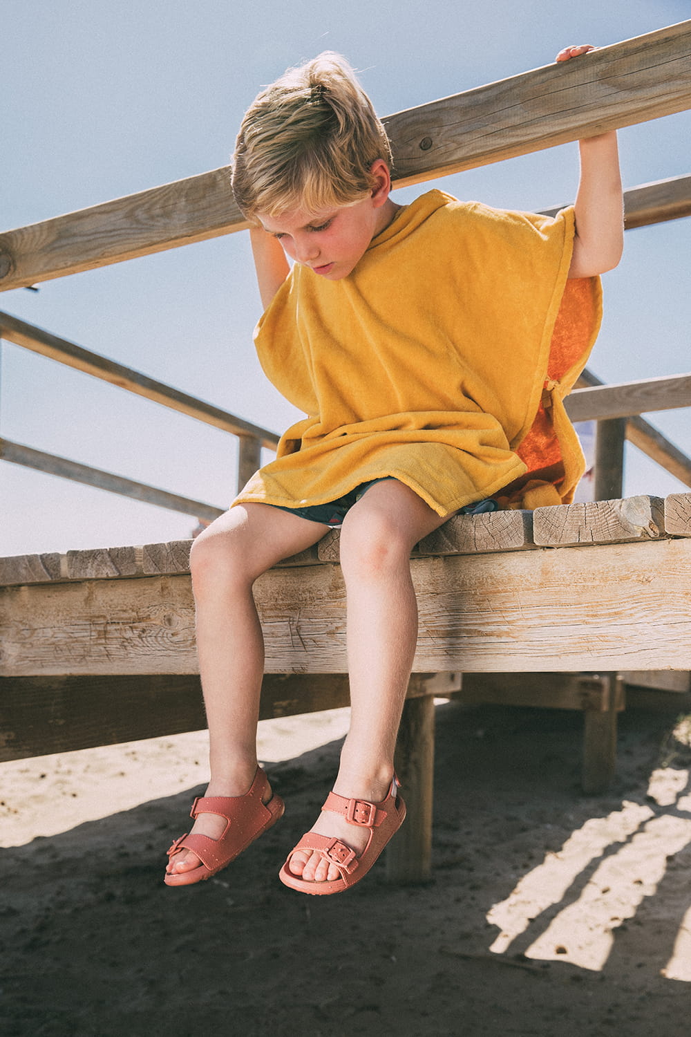Fotografía de moda infantil en exterior con niño luciendo sandalias de verano para campaña de calzado