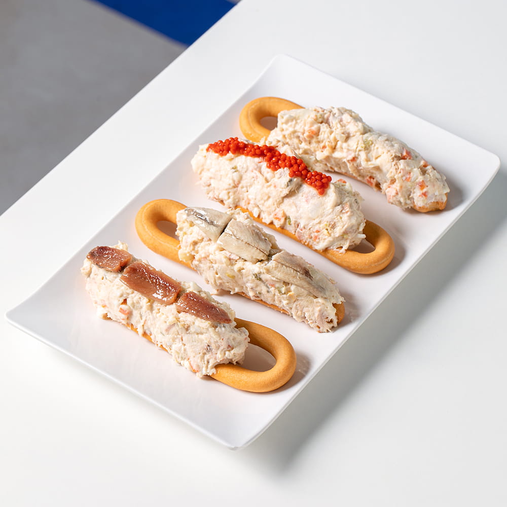Fotografía gastronómica de marineras murcianas de La Boca Te Lía con ensaladilla, anchoa y huevas sobre rosquilla en plato blanco