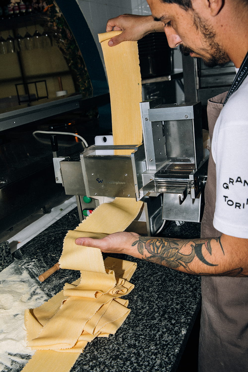 Fotografía gastronómica de chef elaborando pasta fresca con máquina laminadora en cocina profesional de restaurante