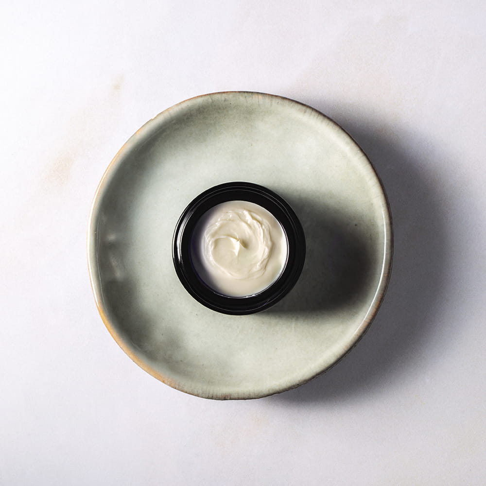 Fotografía de textura de crema Skin Perfection en tarro sobre plato cerámico