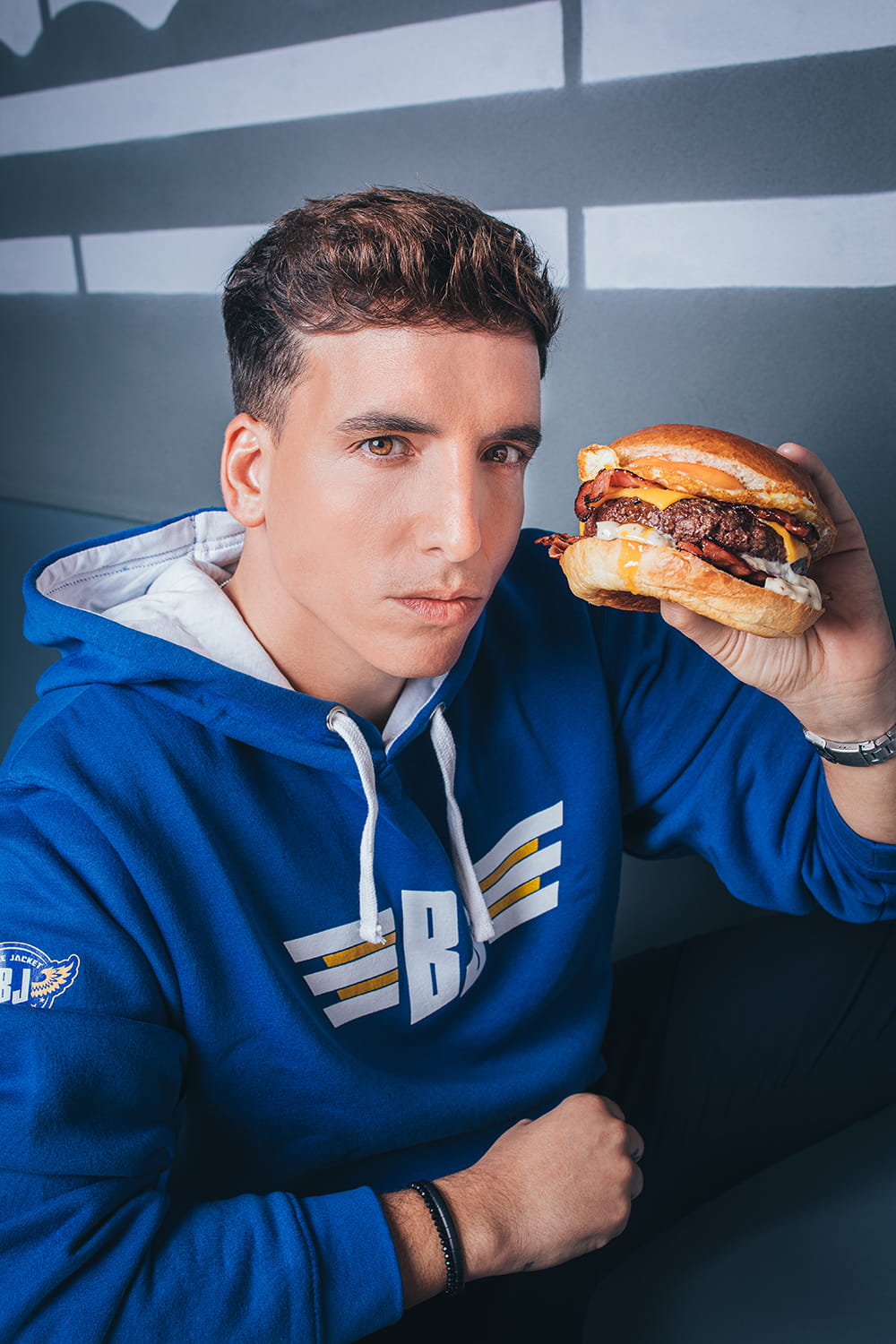 Fotografía publicitaria gastronómica de hamburguesa de La Boca Te Lía sostenida por Xuso Jones en retrato para campaña de marca
