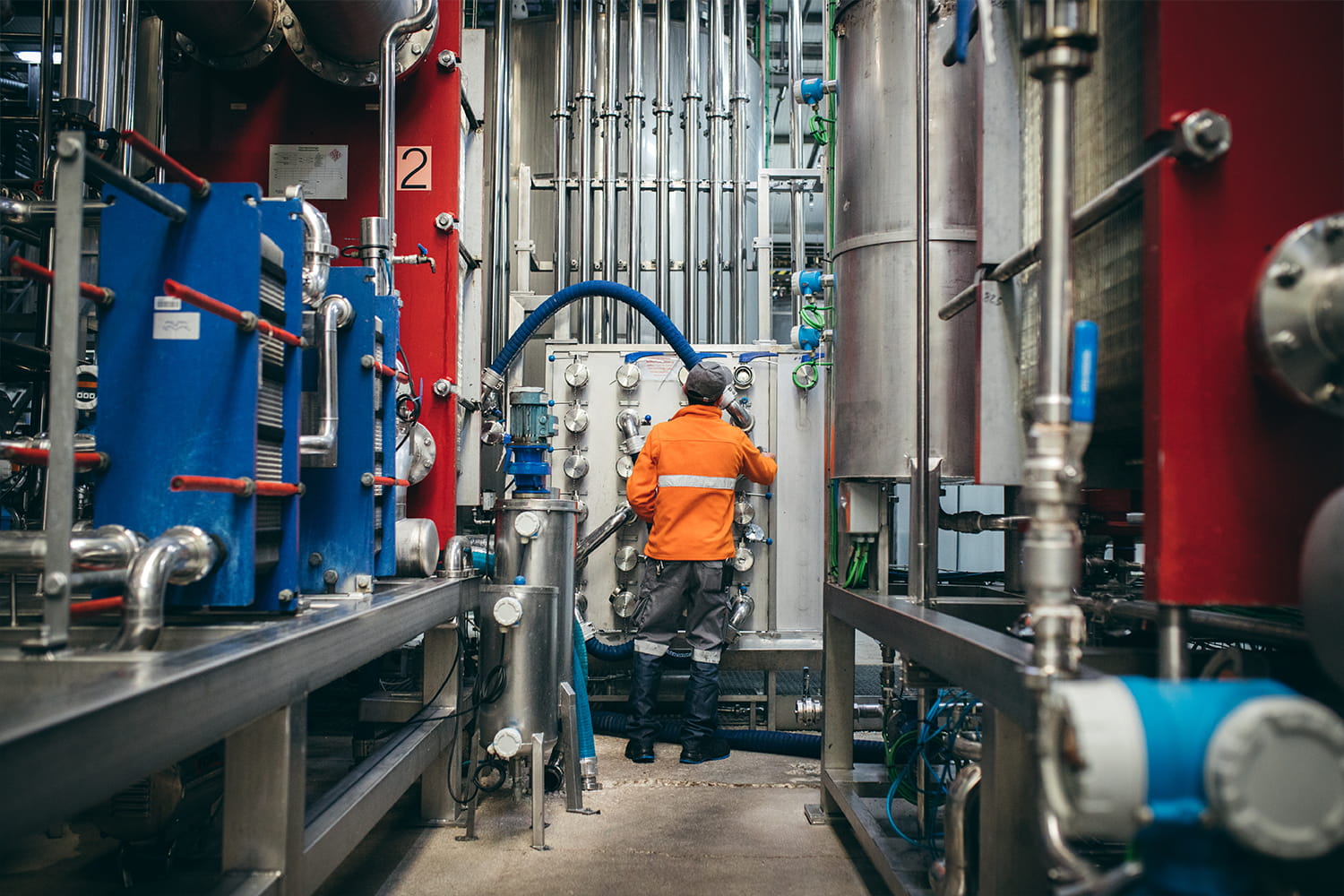 Trabajador en la fábrica de Zukán operando maquinaria industrial entre tuberías y depósitos