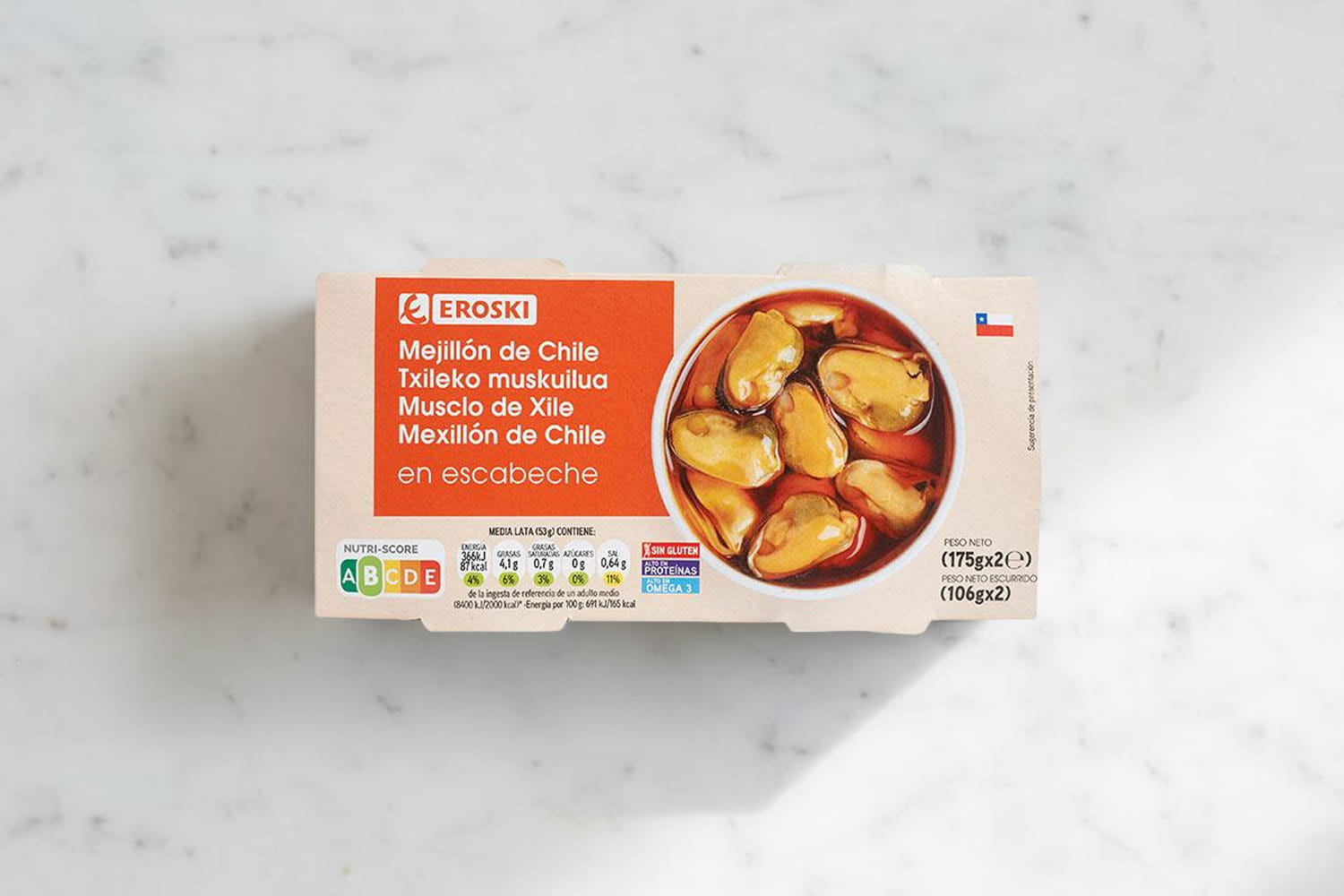 Fotografía de un envase de mejillones en escabeche de Eroski, presentado sobre una superficie de mármol blanco.