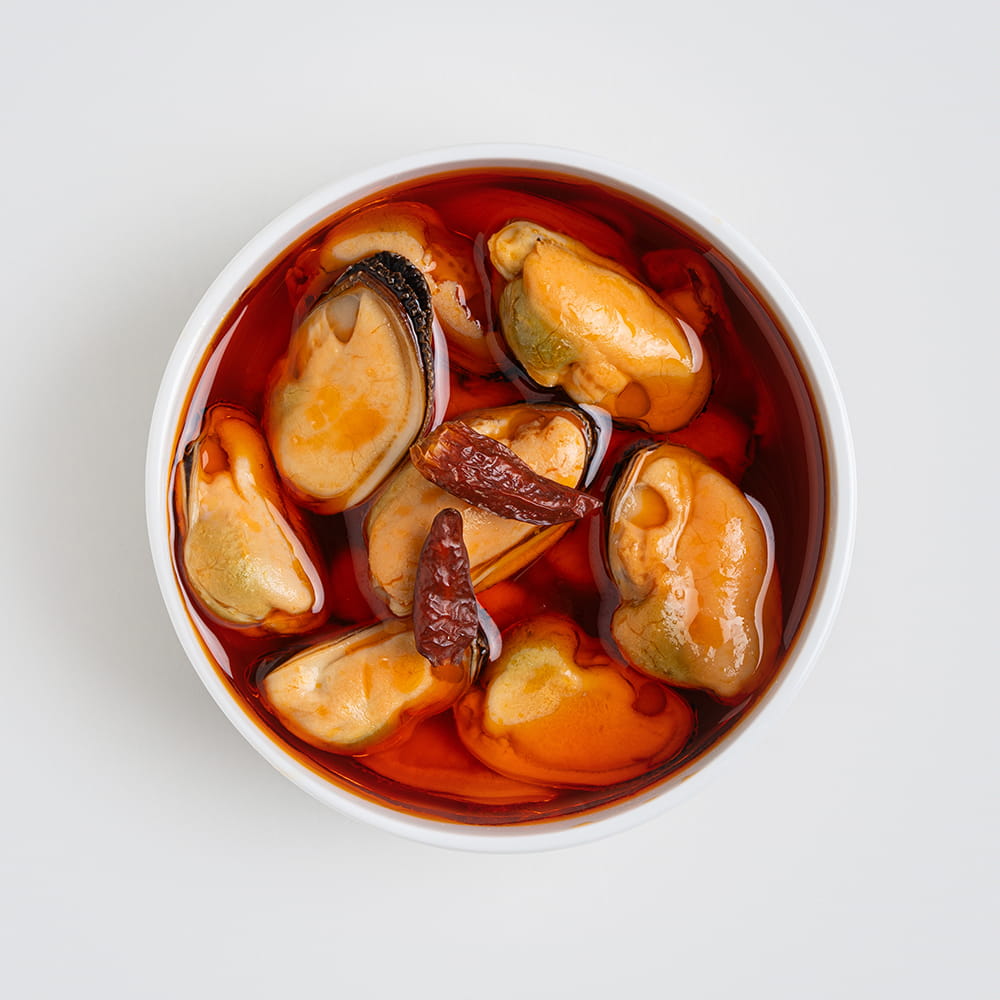 Fotografía cenital de mejillones en escabeche picante con guindilla para packaging de conservas
