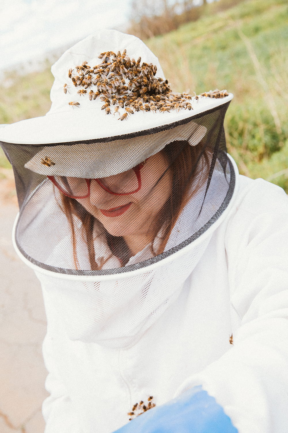 Apicultora con traje protector y abejas sobre el sombrero durante trabajo en colmenas en el campo de Cartagena