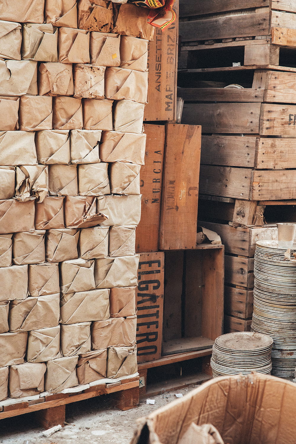 Pilas de paquetes envueltos en papel de estraza junto a cajas de madera antiguas con inscripciones de "Murcia" y "El Gaitero" en la nave de Cristal Antiguo