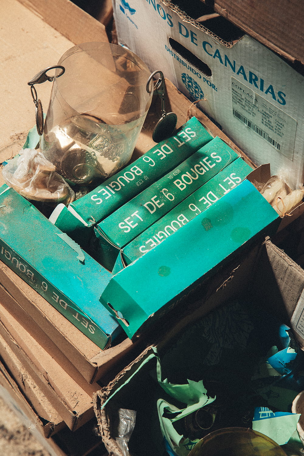 Cajas de cartón antiguas en el almacén de Cristal Antiguo conteniendo sets de velas francesas "Set de 6 bougies" y una cubitera de cristal con detalles dorados, junto a una caja de Plátanos de Canarias