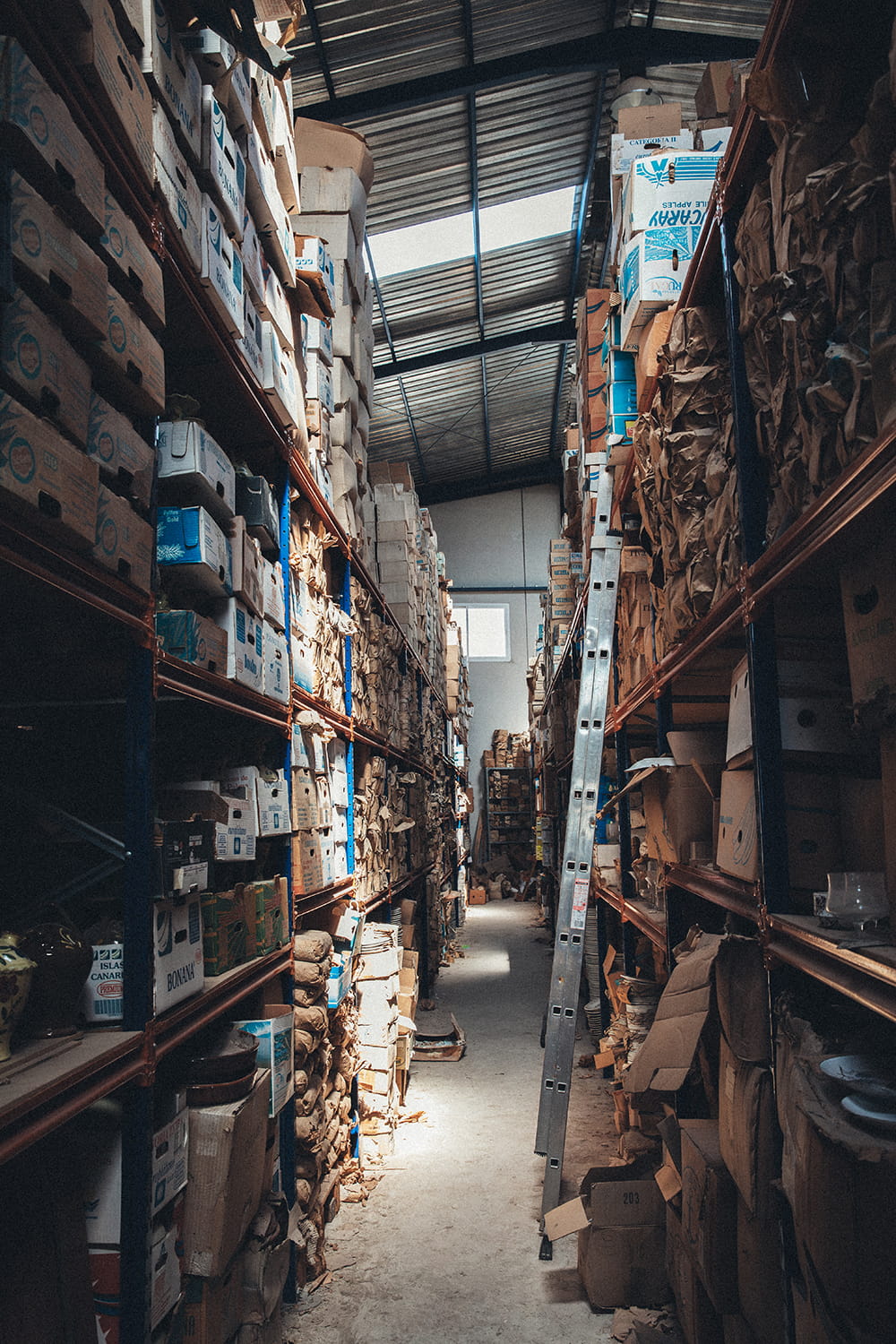 Estanterías industriales de gran altura con cajas de cristal y loza antigua en el almacén de Cristal Antiguo