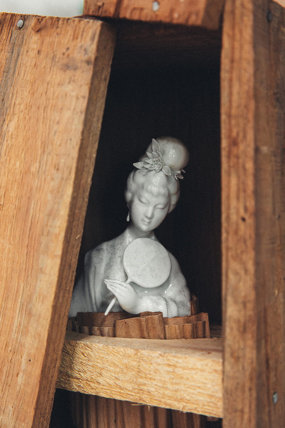 Primer plano del interior de una caja de madera rústica de China, revelando una delicada figura de mujer de porcelana blanca intacta y llena de detalle.