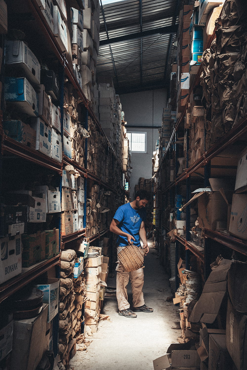 Juan Bohajar examinando una damajuana antigua entre altas estanterías llenas de cajas en el almacén de Cristal Antiguo en Lorquí