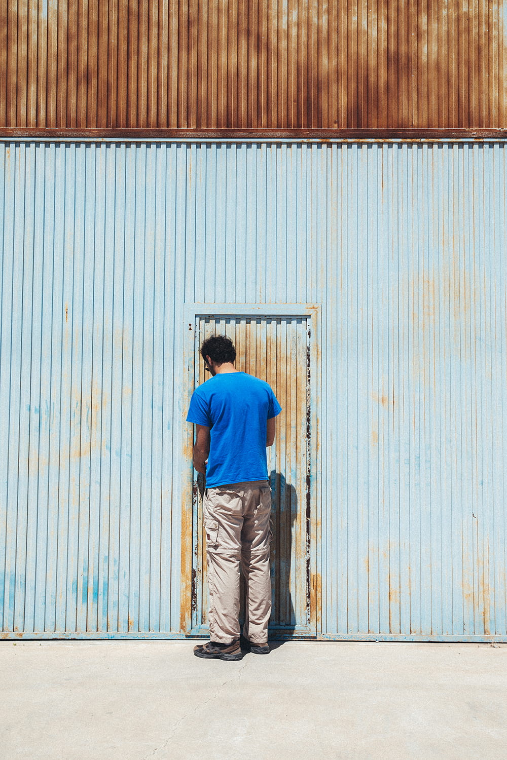 Juan Bohajar, de espaldas, cerrando la puerta metálica oxidada de la nave industrial de Cristal Antiguo en Lorquí, Murcia, al finalizar la visita.