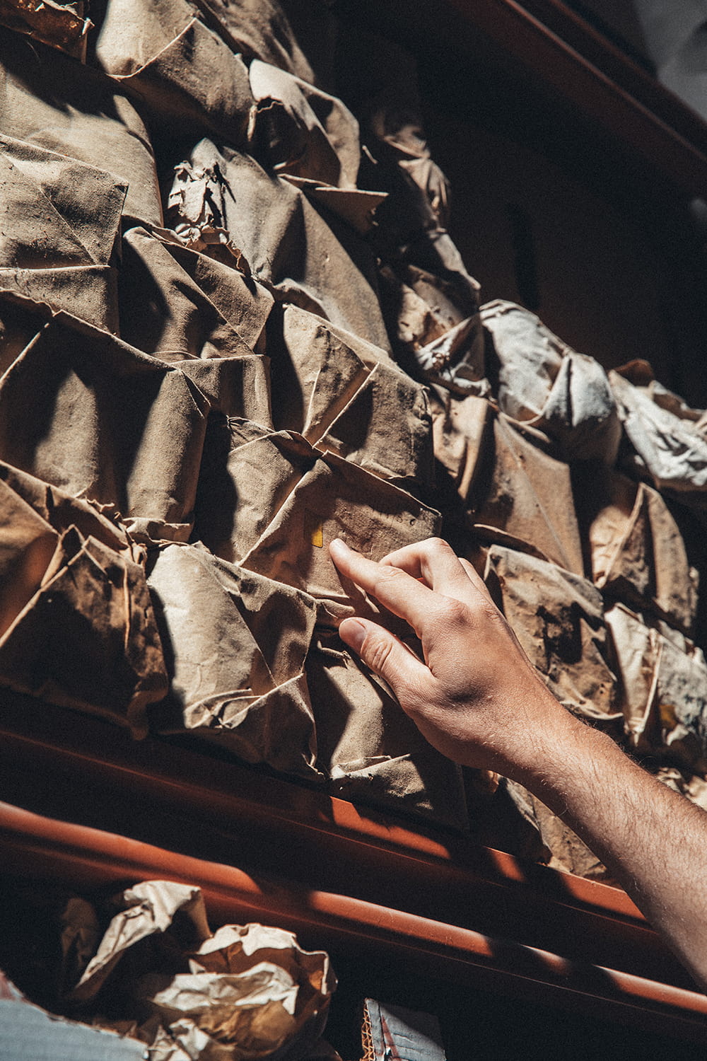 Primer plano de la mano de Juan tocando la textura de un paquete de papel rústico sin abrir en una estantería del almacén de Cristal Antiguo