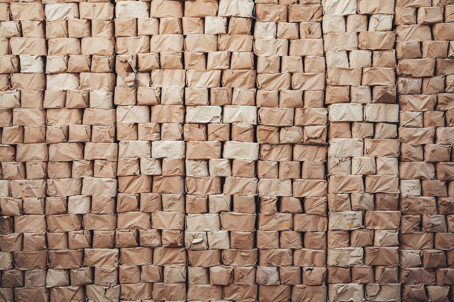 Muro formado por cientos de paquetes de papel rústico apilados, conteniendo stock de menaje antiguo sin abrir en el almacén
