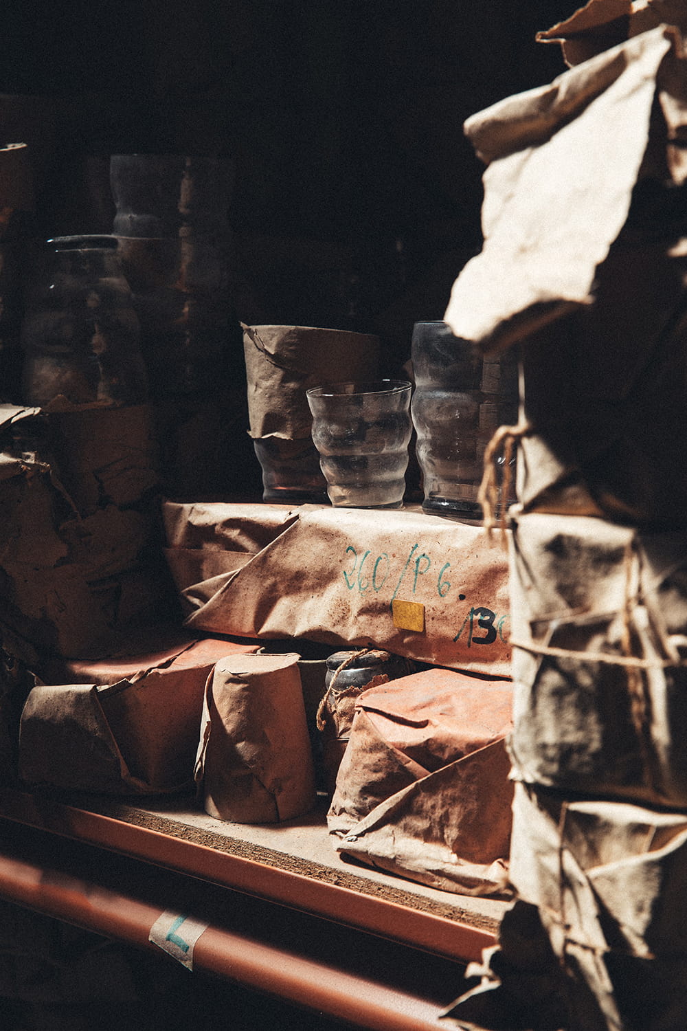 Primer plano en el almacén de Cristal Antiguo de paquetes de vidrio rústico sin abrir, atados con cuerda y marcados a mano, junto a vasos de cristal expuestos